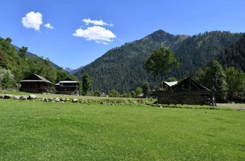 a group of buildings in a green field with mountains at Keran resort in Keran