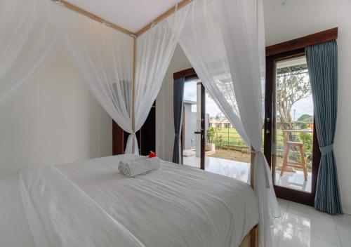 a bedroom with a bed with white sheets and curtains at Putra House Ubud in Ubud
