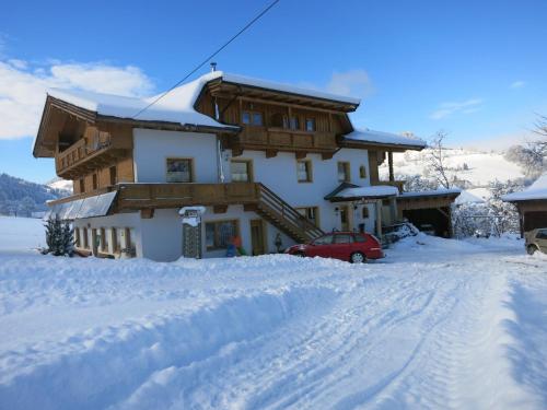 a snow covered house with a red car in front of it at Ferienwohnungen Marchanger in Niederau