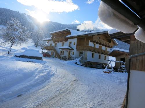 a house in the snow with the sun in the background at Ferienwohnungen Marchanger in Niederau