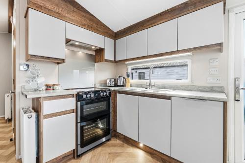 a kitchen with white cabinets and a stove at Harbour View at Avocet Crescent - Luxury Lodge with Hot Tub - Hayling Island - Mill Rythe Holiday Village in North Hayling