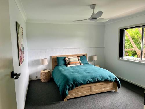 a bedroom with a bed with a blue comforter and a window at Cedarvale Cottage in Boambee