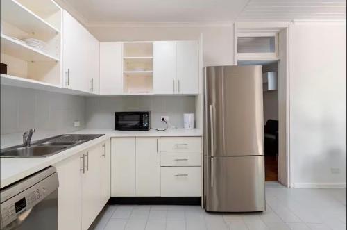a kitchen with white cabinets and a stainless steel refrigerator at Cosy Cottage in Annandale in Sydney