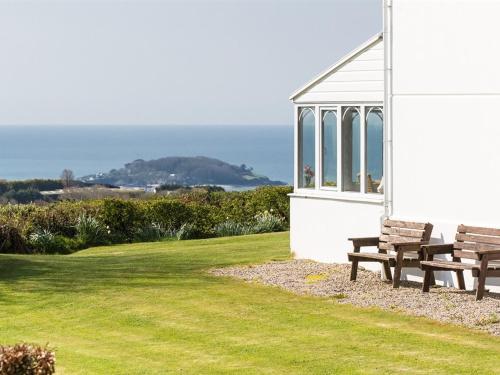 two wooden benches sitting next to a white building at Bucklawren Farm in Looe