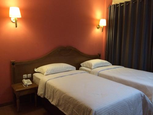 two beds in a hotel room with two lamps at Nina Hotel Syariah in Salatiga