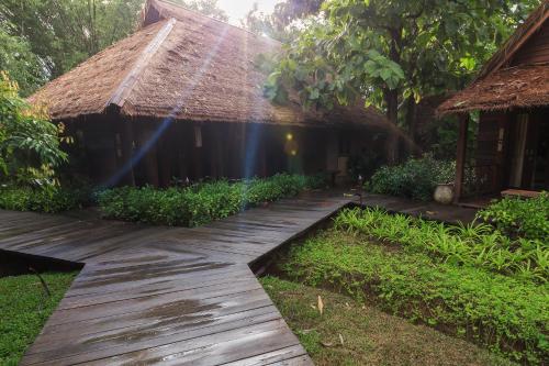 a wooden pathway leading to a hut with a thatched roof at Azalea Village in Chiang Dao