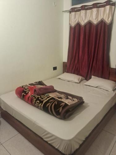 a bed with a blanket on it with a red curtain at Krishna Homestay in Bhowāli