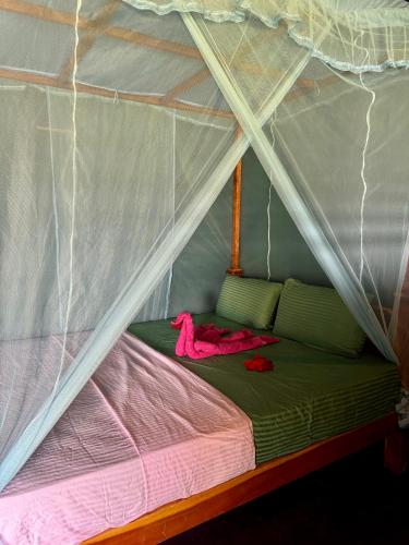 a canopy bed in a tent with pink sheets at Lakeview Birdsong Cabanas in Debarawewa