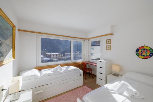 a white bedroom with two beds and a window at Brentsch A27 in Scuol