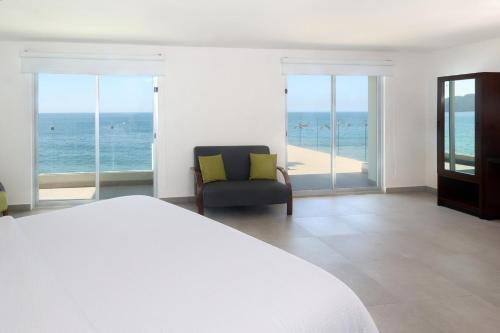 a bedroom with a bed and a chair and the ocean at Garner Hotel Mazatlan Beach by IHG in Mazatlán