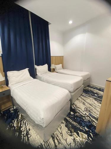 two beds in a room with blue curtains at فندق اوتاد المتحدة المعابدة in An Naqāʼ