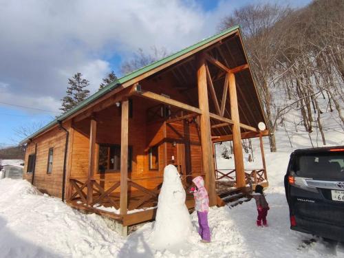 a family standing in front of a log cabin in the snow at 源泉ログの宿 in Sobetsu