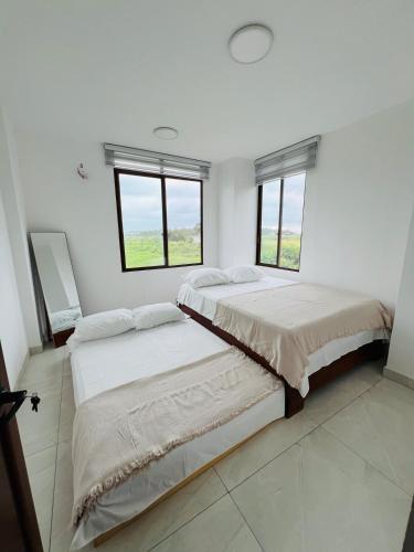 two beds in a white room with two windows at Cesar Palace Departamento in Cojimíes