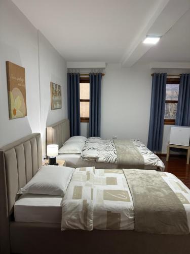 two beds in a bedroom with blue curtains at Bujtina Kenedi in Korçë