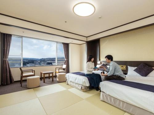 a man and woman sitting on beds in a hotel room at KAMENOI HOTEL Ichinoseki in Ichinoseki