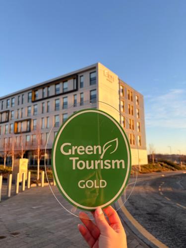 a person holding a green tourism gold sign in front of a building at Aloft by Marriott Aberdeen TECA in Aberdeen