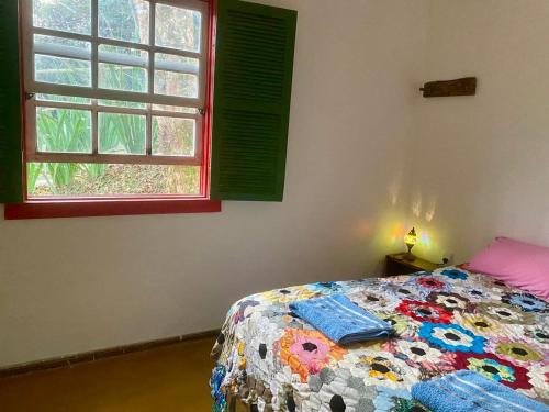 a bedroom with a bed with a colorful blanket and a window at Chalé na floresta com varanda in Ouro Preto