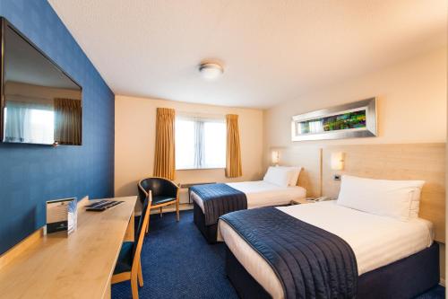 a hotel room with two beds and a desk at Leonardo Inn Aberdeen Airport in Dyce