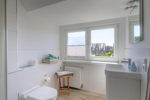 a bathroom with a toilet and a sink and two windows at Ferienwohnung-NEU-Weidenstieg-OG in Wenningstedt