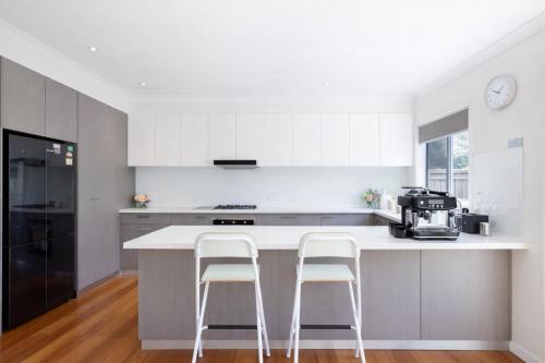 a kitchen with a white counter and two stools at Welcome home Burwood in Burwood