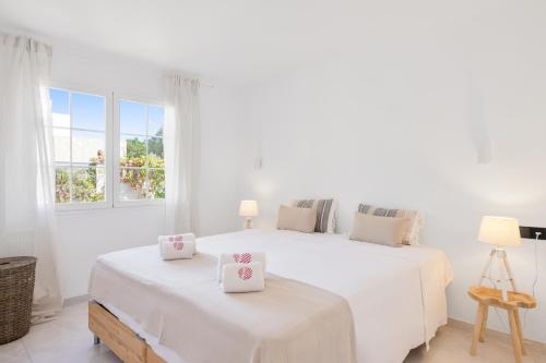 a white bedroom with two beds and two windows at Villa Sa Sirvi in Santa Ponsa