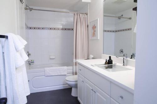 a white bathroom with a tub and a toilet and a sink at Lakefront Haven Mtn View Condo Steps from Beach in Harrison Hot Springs
