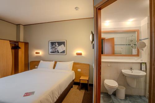 a bedroom with a bed and a bathroom with a sink at Tulip Inn Turin South in Moncalieri