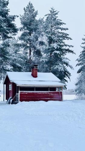 a red barn with a snow covered roof in a field at Savupirtti 1819 in Pudasjärvi
