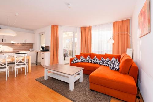 a living room with an orange couch and a table at Strandhaus Lobbe, Sanddorn Nr 3 - Bade- & Saunawelt täglich inklusive in Lobbe