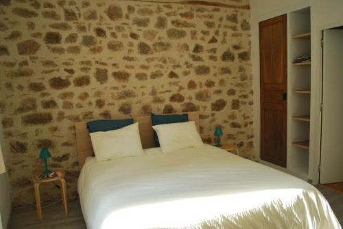 a bedroom with a white bed with a stone wall at Maison Le Feu Follet in Lormes