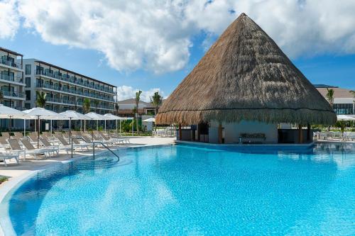 a swimming pool with chairs and a thatch roof at Ocean Allure Costa Mujeres - Adults Only - All Inclusive in Costa Mujeres