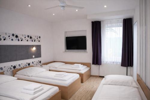ein Zimmer mit drei Betten und einem Flachbildfernseher in der Unterkunft Pension Central Nuernberg-Fuerth in Fürth
