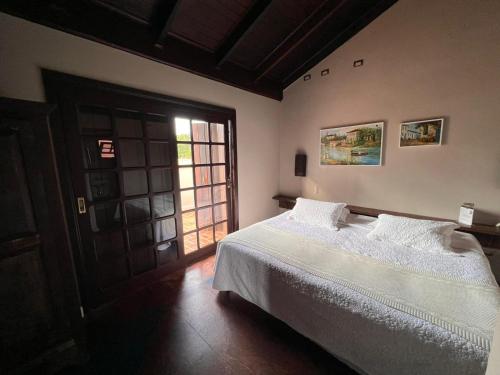 a bedroom with a bed with white sheets and a window at Casa 1915 Pousada in Morretes