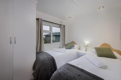 two beds in a white room with a window at Tranquil Lodge with river views in Hambleton