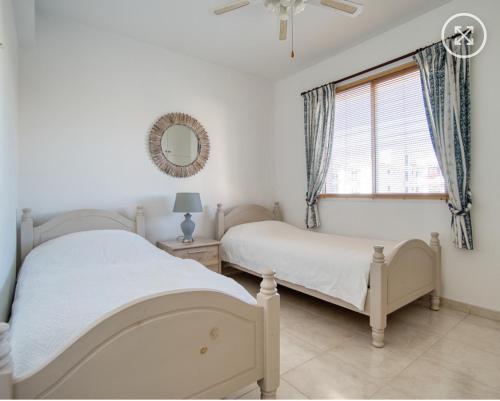 two beds in a bedroom with a window and a mirror at Newly Renovated Light House Beach 8 min in Paphos