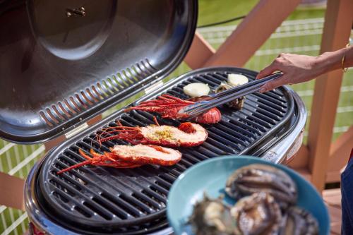 a person cooking food on a grill with tongs at Solana木更津 in Kisarazu