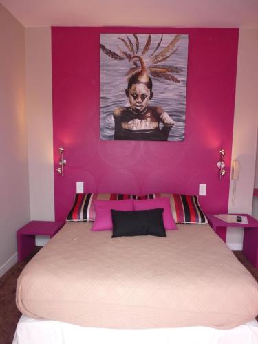a bed with a pink wall with a painting above it at Hôtel Patton in Avranches