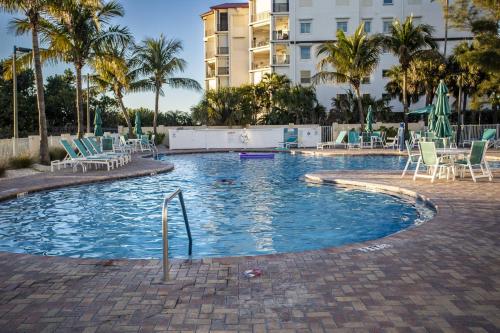 a swimming pool with chairs and palm trees and a building at 501-S - Sunset Vistas in St. Pete Beach