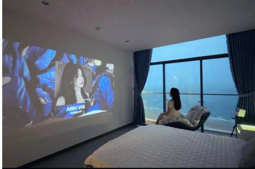 a woman sitting in a chair in a bedroom with a large window at CSJ Tower Seaview Apartment -Luxury Near Back Beach Vung Tau City in Vung Tau