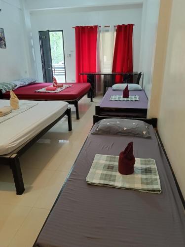 three beds in a room with red curtains at Chelle's apartelle-inn in El Nido