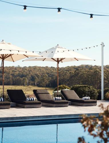 a group of lounge chairs and umbrellas next to a pool at The Oaks Ranch in Tomakin