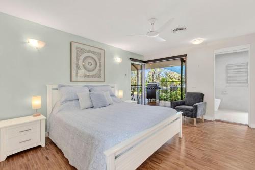 a white bedroom with a bed and a chair at Sunsets on Kalang in Urunga