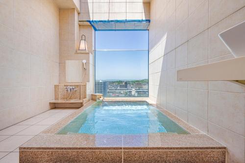 a large swimming pool in a bathroom with a window at Candeo Hotels Fukuyama in Fukuyama