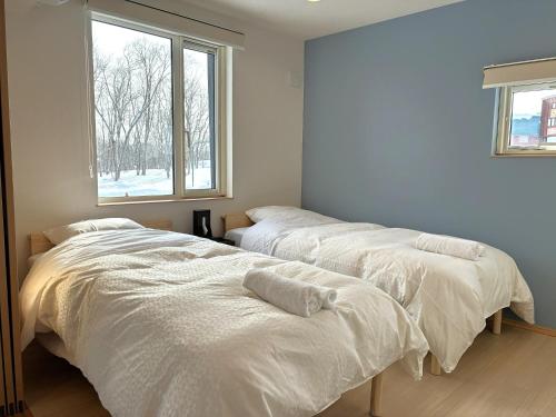two white beds in a room with a window at ニセコ泉居アパートメント in Kutchan