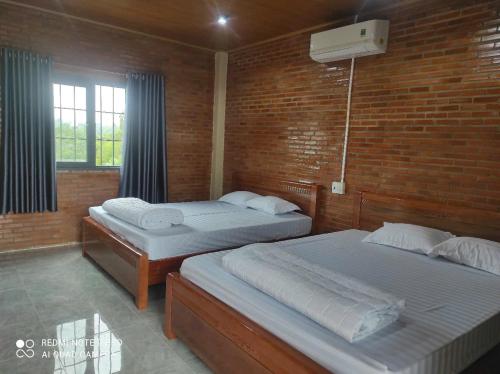two beds in a room with a brick wall at Cat Tien Riverside Lodge in Tân Phú