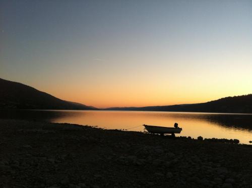 a boat sitting on the shore of a lake at sunset at HOTEL de la Truite & SPA Le petit Nautilus in Le Pont