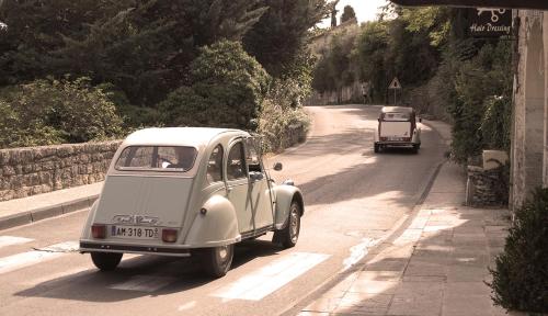 an old white car driving down a road with a truck at Cyprès du Paradis à Gordes in Gordes