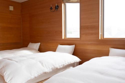two beds in a room with wooden walls and windows at Kaitan稲佐の浜 in Taisha