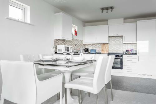 a white kitchen with a table and white chairs at Beach Point - Stunning Harbour Views from Balcony in Poole