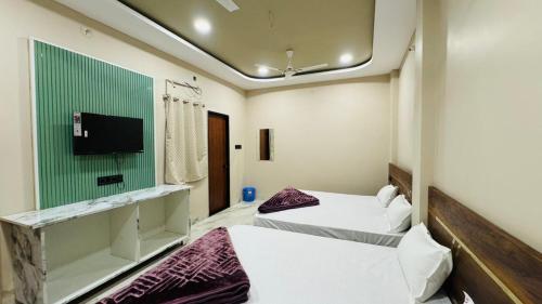 two beds in a room with a tv on the wall at Hotel Shri Kaila Devi in Ujjain
